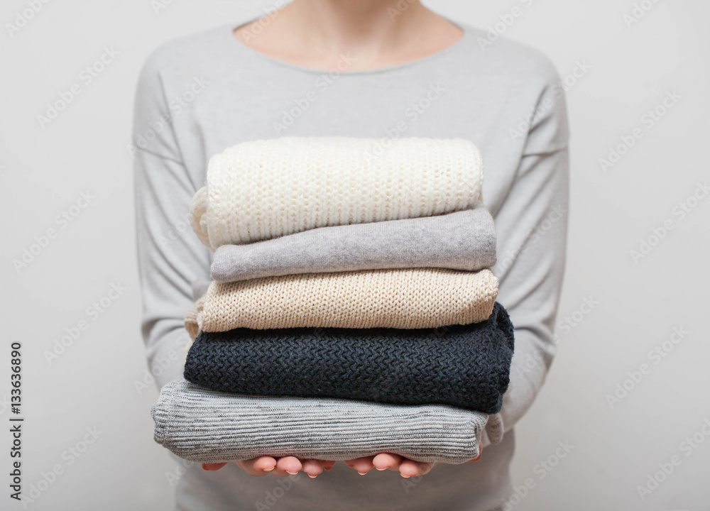 Woman holding stack of sweaters on grey background Woman holding stack of sweaters on grey background