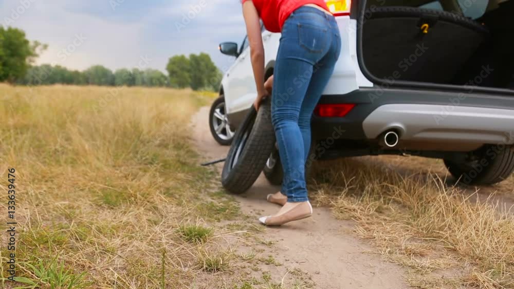 Young woman taking out spare wheel out of the car and rolling it on ground Young woman taking out spare wheel out of the car and rolling it on ground