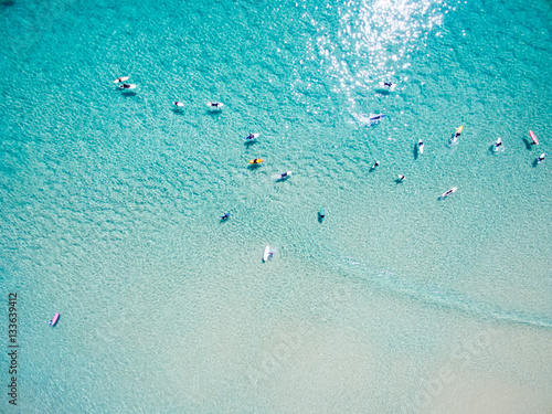 An aerial view of surfers waiting for a wave in the ocean on a clear day