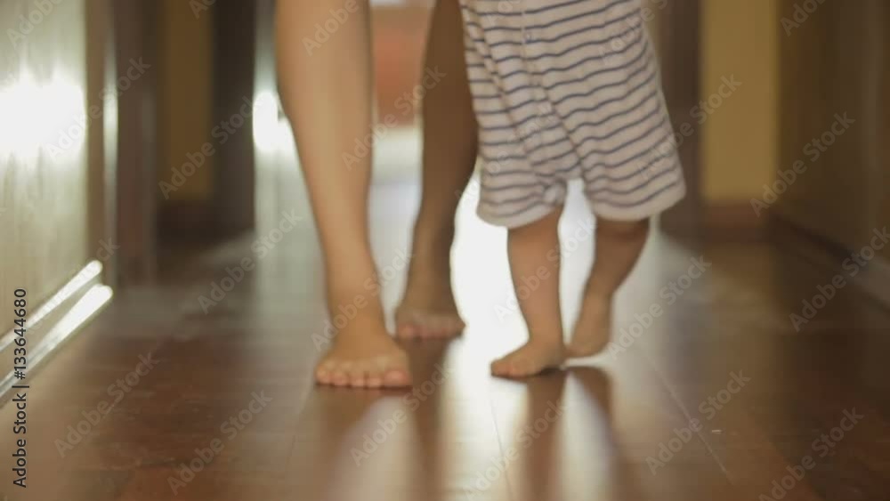Closeup of mothers and baby's feet walking on wooden floor at long hallway Closeup of mothers and baby's feet walking on wooden floor at long hallway