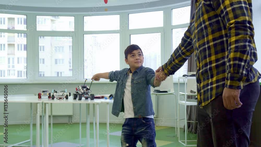 Little brunette boy pulling his father to play with him. Son holding man's hand against background of windows. Male child wants to entertain with toys Little brunette boy pulling his father to play with him. Son holding man's hand against background of windows. Male child wants to entertain with toys