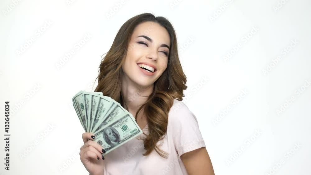 Happy young woman holding money in her hands and pointing finger at camera while standing isolated on white Happy young woman holding money in her hands and pointing finger at camera while standing isolated on white