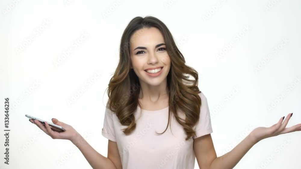 Happy young woman looking at mobile phone and smiling while standing against white background Happy young woman looking at mobile phone and smiling while standing against white background