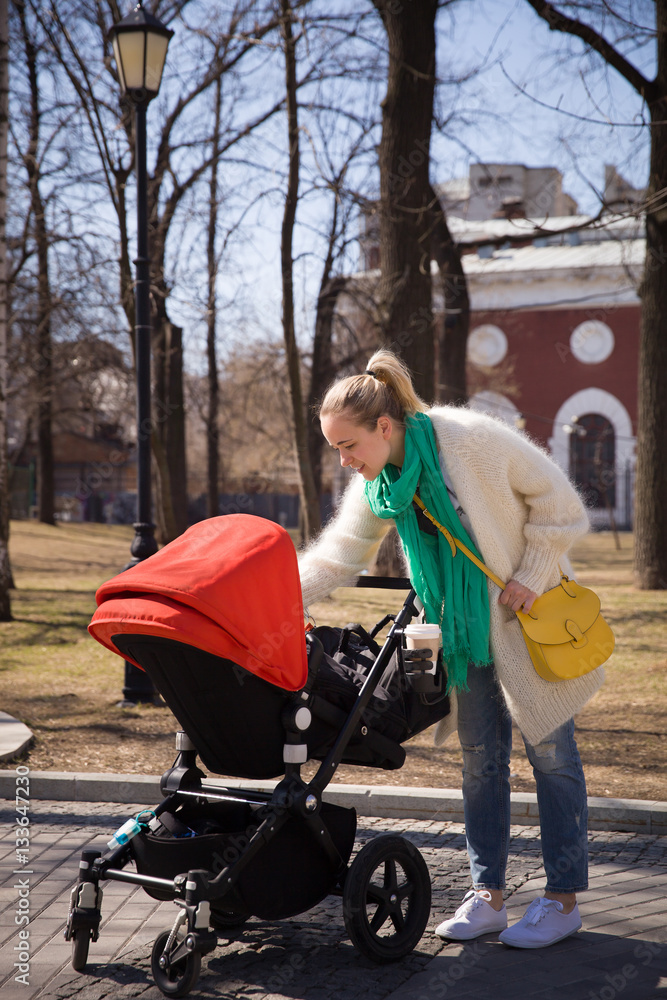 Young happy woman walking with stroller in the city. Mother with baby child in a pram. Lifestyle concept Young happy woman walking with stroller in the city. Mother with baby child in a pram. Lifestyle concept