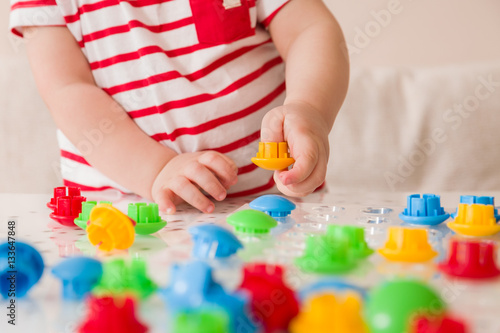 Closeup of child's hand taking bright mosaic parts. Playing and learning colors at home. Toddler boy in a striped shirt playing with colorful constructor details. Activities with children