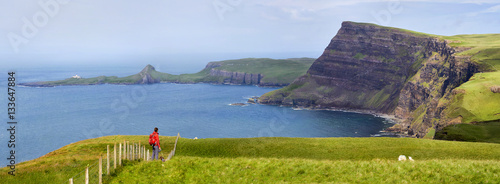 A hiker and their dog on the sea cliffs of Ramasaig with Neist Point in the distance. Isle of Skye, Scotland, UK.       photo