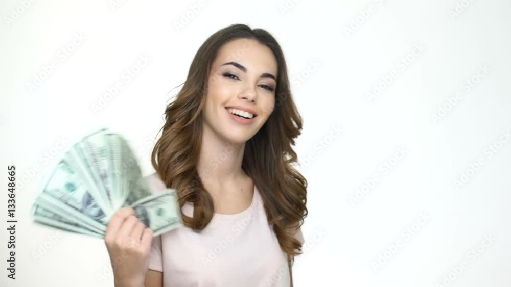 Satisfied young woman holding fan of money banknotes in her hands and looking at camera while standing isolated on white Satisfied young woman holding fan of money banknotes in her hands and looking at camera while standing isolated on white