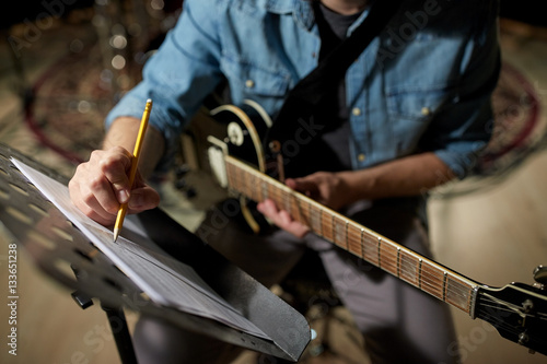 man with guitar writing to music book at studio