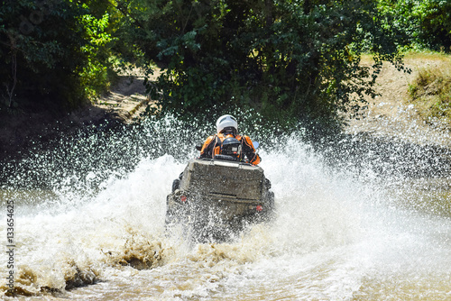 The man on the ATV crosses a stream. Tourist walks on a cross-country terrain photo