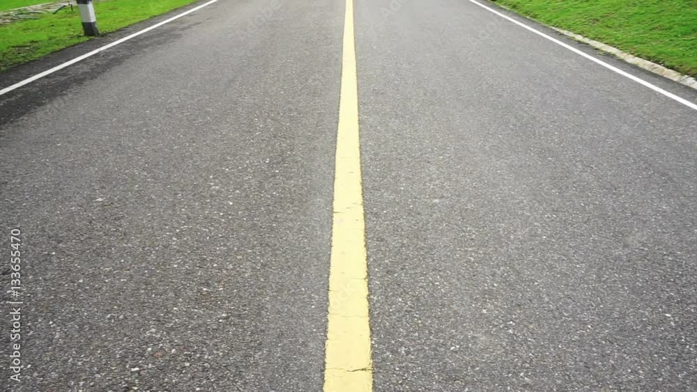 Asphalt road perspective with yellow line panning up. Guiding way to surround by with green nature Asphalt road perspective with yellow line panning up. Guiding way to surround by with green nature