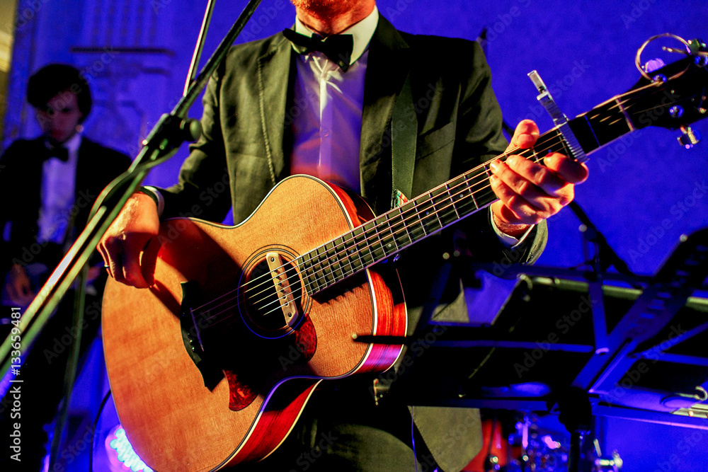 Obraz premium Man in black suit plays a guitar standing on the stage illuminat