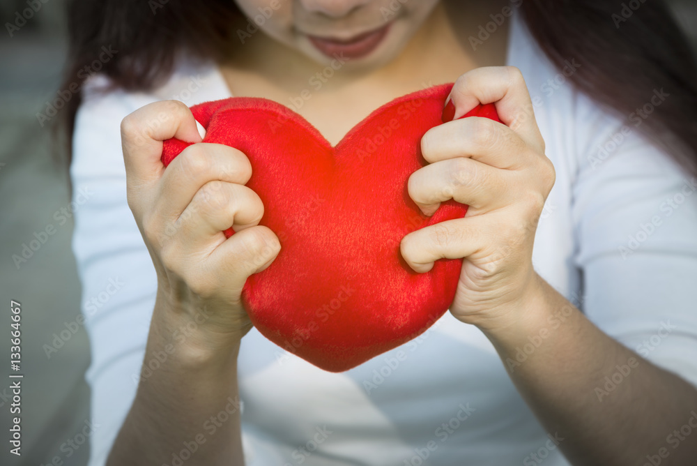 Asian lady hands holding red soft heart small pillow tightly to show her strong feeling of love on Valentines day, soft sunlight and selective focus Asian lady hands holding red soft heart small pillow tightly to show her strong feeling of love on Valentines day, soft sunlight and selective focus