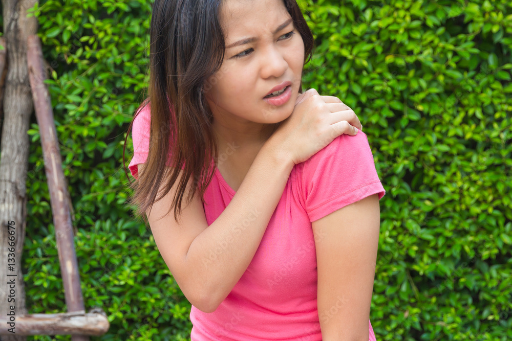 Young woman shoulder or joint pain in garden, injury concept.