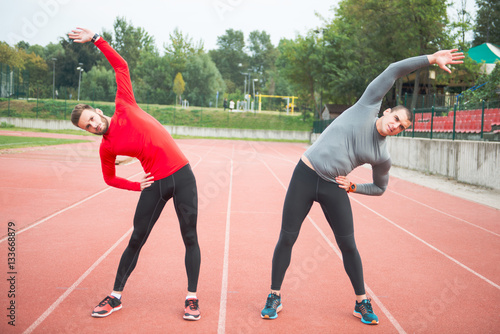 Warming up on a race track. Two friends stretching before a run.