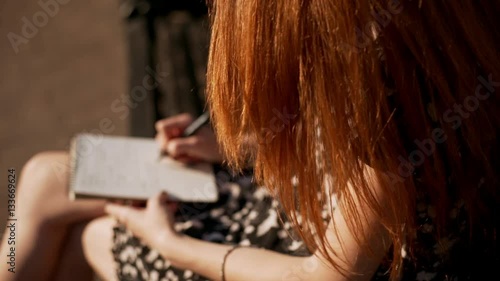 Redhead young girl gently writing notes while wind slightly blowing her hairin slowmotion photo