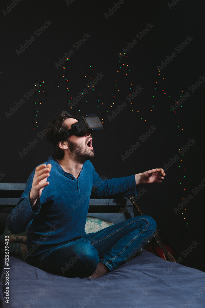 Young man wearing virtual reality glasses and sitting on sofa in a room Young man wearing virtual reality glasses and sitting on sofa in a room