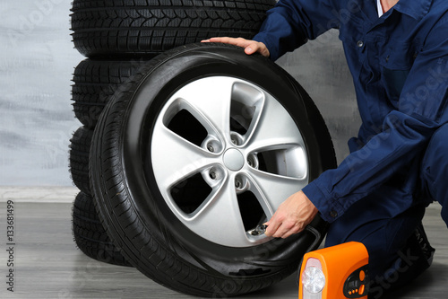 Young mechanic in uniform with wheels, on gray background