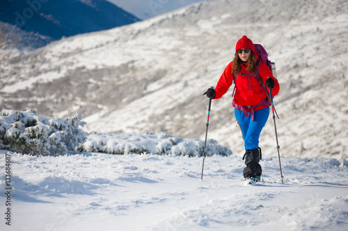 Girl with backpack walking on snow in the mountains. © zhukovvvlad