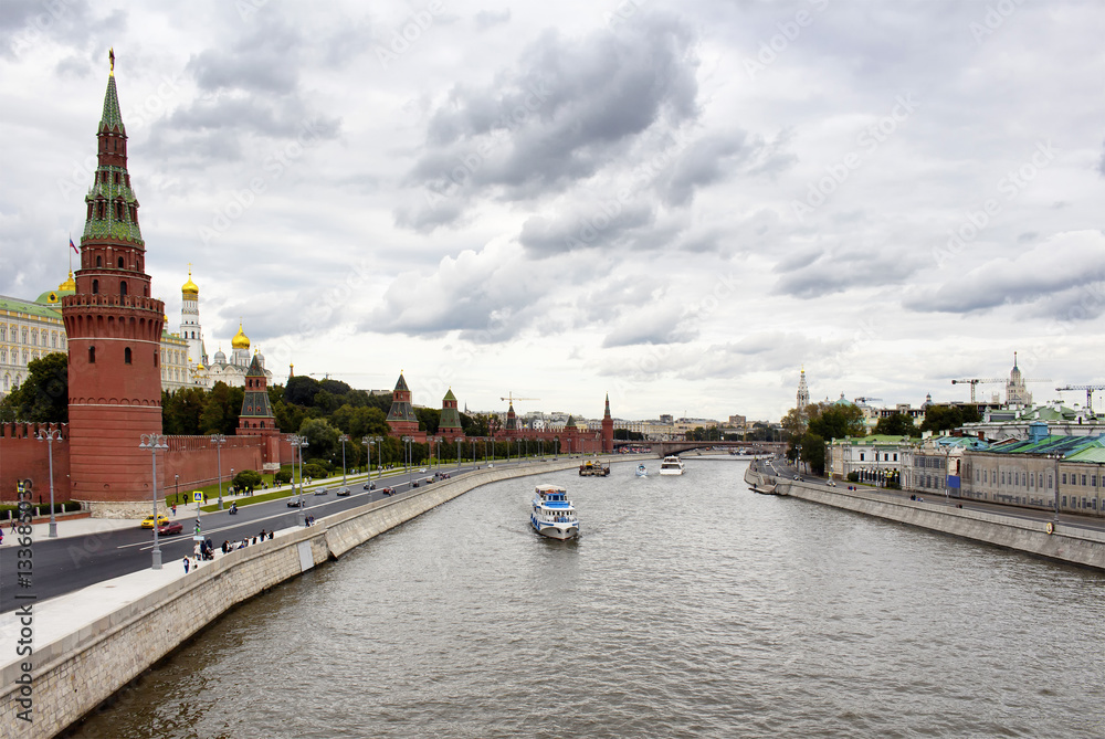 Tour boats / ships are on Moskva river. Dramatic cloudy sky is in the view. Dormition Cathedral, Kremlin Palace and Borovitskaya Tower are on the left side of the image.