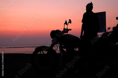 Young man standing near motorbike and enjoying sunset view 