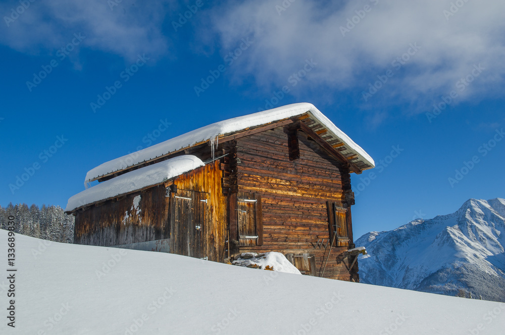 winter landscape with an old wooden cottage in front of a mountain range
