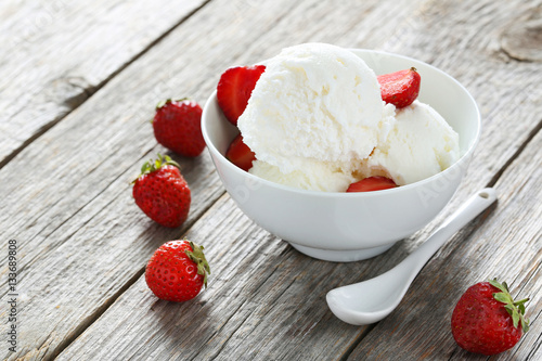 Ice cream in bowl with strawberries on grey wooden background