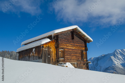 winter landscape with an old wooden cottage in front of a mountain range 