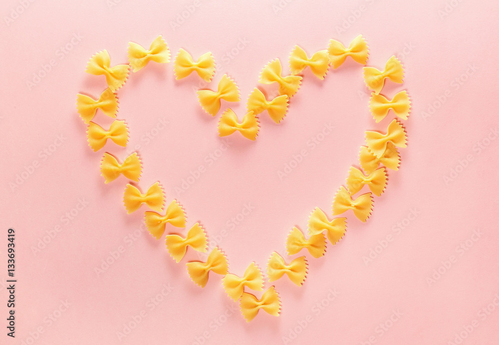 Heart frame from wheat pasta farfalle on rose background. Valentine's day.