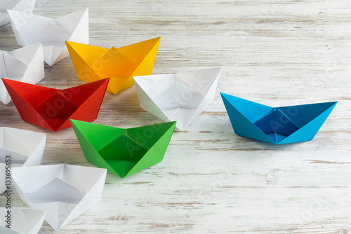 Business leadership concept with white and color paper boats on wooden table