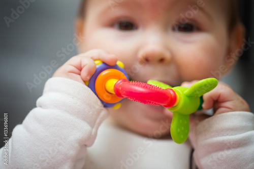 Eight months old baby girl sucking her red, green and orange toy