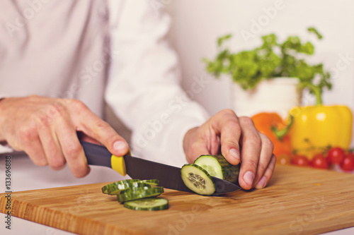Chef's hands. Man is ready to prepare fresh salad. Chopping cucumber.
