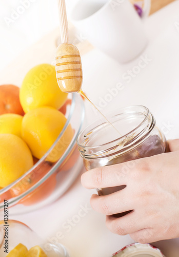 Close up of hands with honey dipper in the air and citrus fruits served on wooden tray