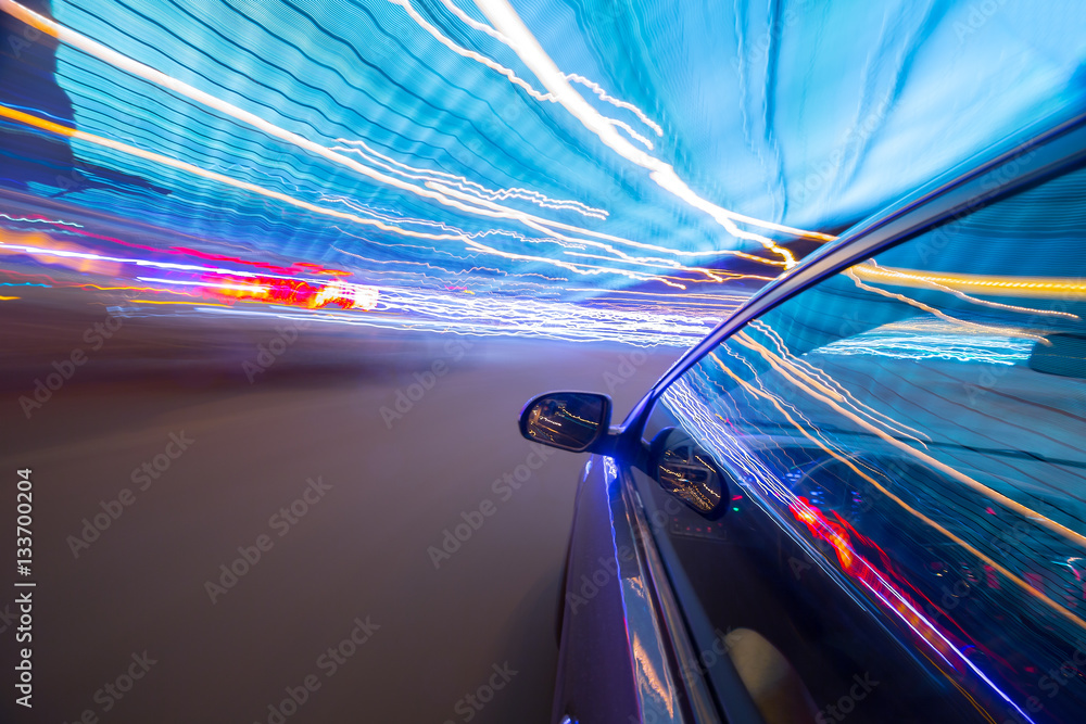 Obraz premium View from Side of Car moving in a night city, Blured road with lights with car on high speed. Concept rapid rhythm of a modern city.