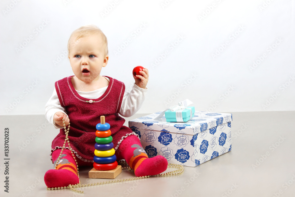 Unhappy angry little baby girl sitting alone with presents and toys. Unhappy angry little baby girl sitting alone with presents and toys.