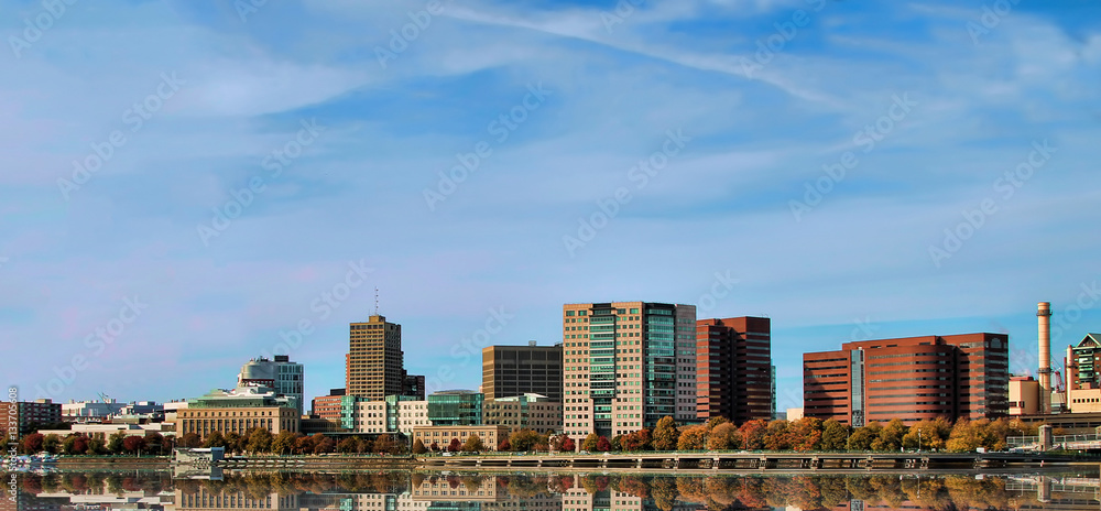 Photo of a cityscape of Boston across a river with reflections of buildings. Photo of a cityscape of Boston across a river with reflections of buildings.