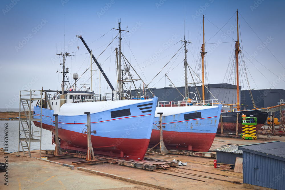 Sail boat with workers in a boatyard being repaired Sail boat with workers in a boatyard being repaired