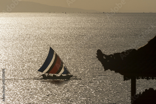 Balinese Fishing Boat. A Bali fishing boat, called a jukung, sails past a Hindu temple roof on the way to the beach to unload the catch of the day-usually mackerel or barracuda, during a sunrise. photo