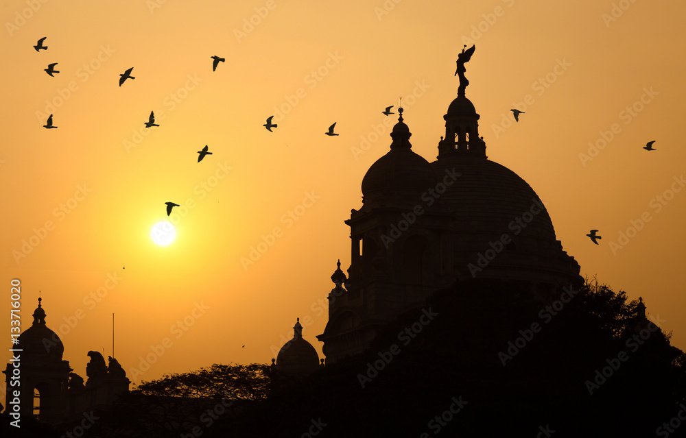 Silhouette Victoria Memorial architectural dome at sunset with flying birds.