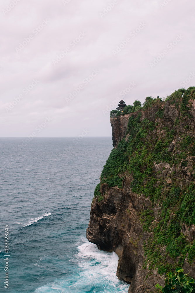 The pictersque rock in the ocean with the temple on te top. Azure waves with white foam of Indian ocean, Indonesia, Bali, Uluwatu