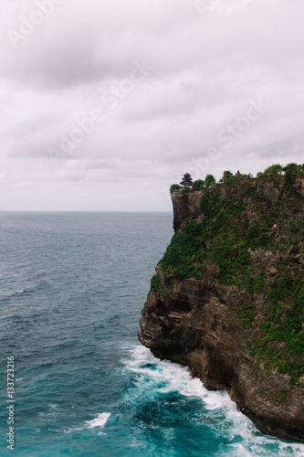 The pictersque rock in the ocean with the temple on te top. Azure waves with white foam of Indian ocean, Indonesia, Bali, Uluwatu photo