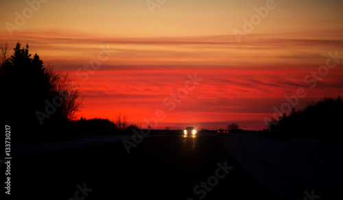 Headlights and taillights travelling along a highway at night under an orange sunset in rural landscape