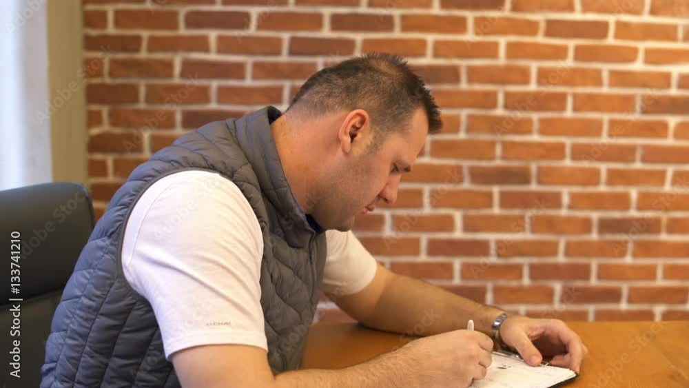 Young man working in modern office writing note and he looks at the camera Young man working in modern office writing note and he looks at the camera