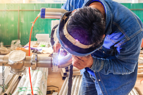 Industrial worker with protective mask welding metal piping using tig welder photo