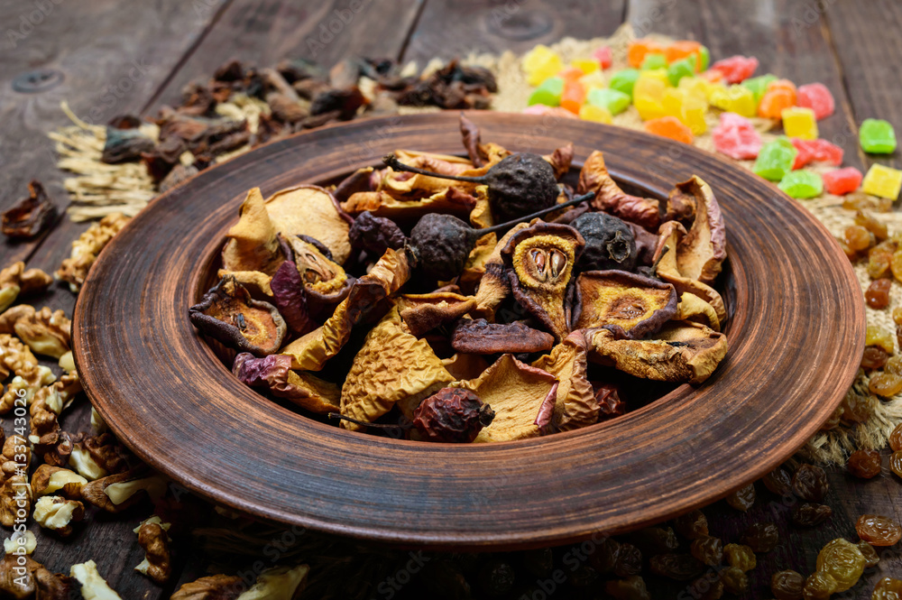 Dried fruit (apples, pears, apricots), berries, raisins and nuts in a bowl on dark wooden background. Close up. Ingredients for the winter vitamin drink, compote.