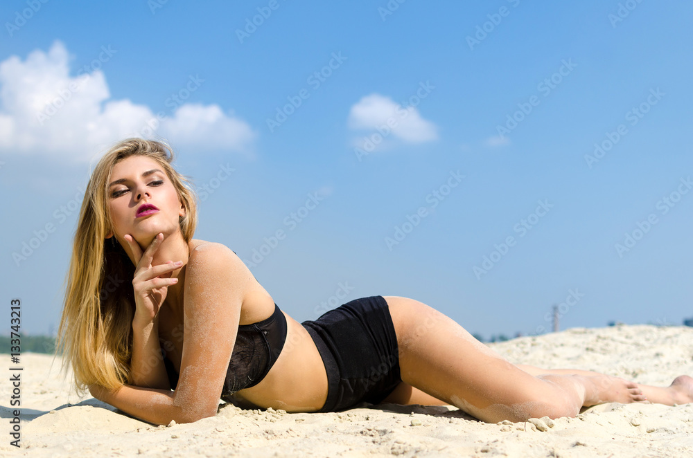 Luxury blond in black lingerie lying on a sandy beach