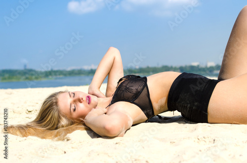 Luxury blond in black lingerie lying on a sandy beach