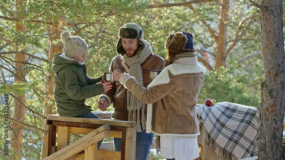 Parents and little boy relaxing in wooden alcove in forest in winter drinking tea and laughing Parents and little boy relaxing in wooden alcove in forest in winter drinking tea and laughing