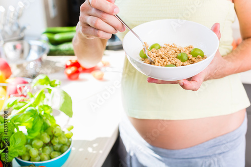 Frau ist schwanger und isst gesundes Müsli mit Obst in ihrer Küche daheim