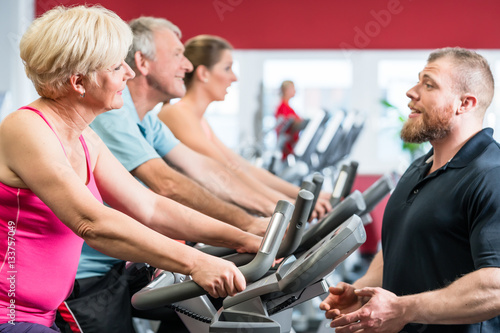 Personal trainer instructs senior woman about spinning at the gym