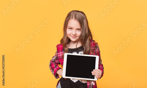 little girl showing blank black tablet pc on yellow background